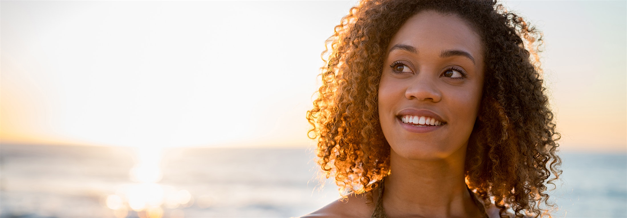 Woman with curly hair at the beach with the sunset in the background