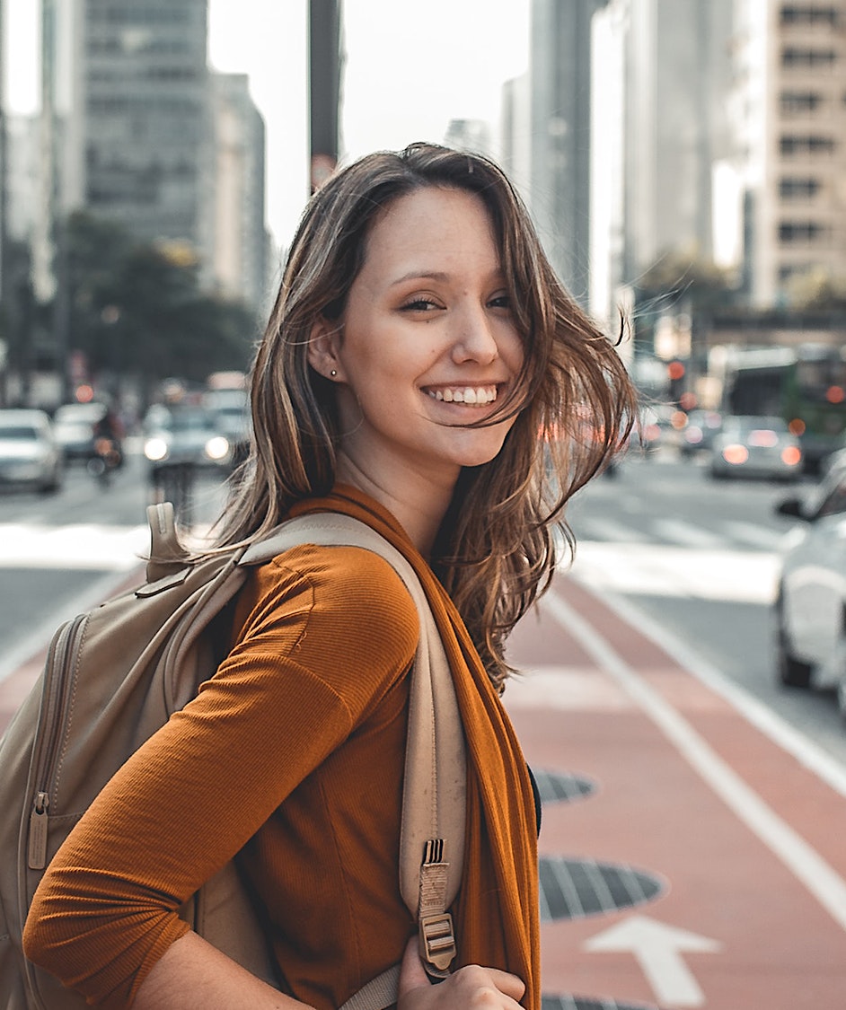 smiling woman with backpack on city street with cars in background