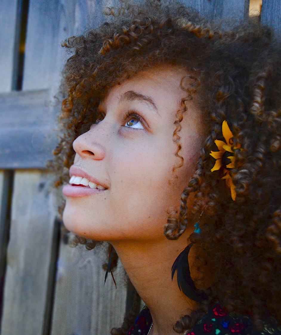 Woman with curly hair looking up with a sunflower behind her ear