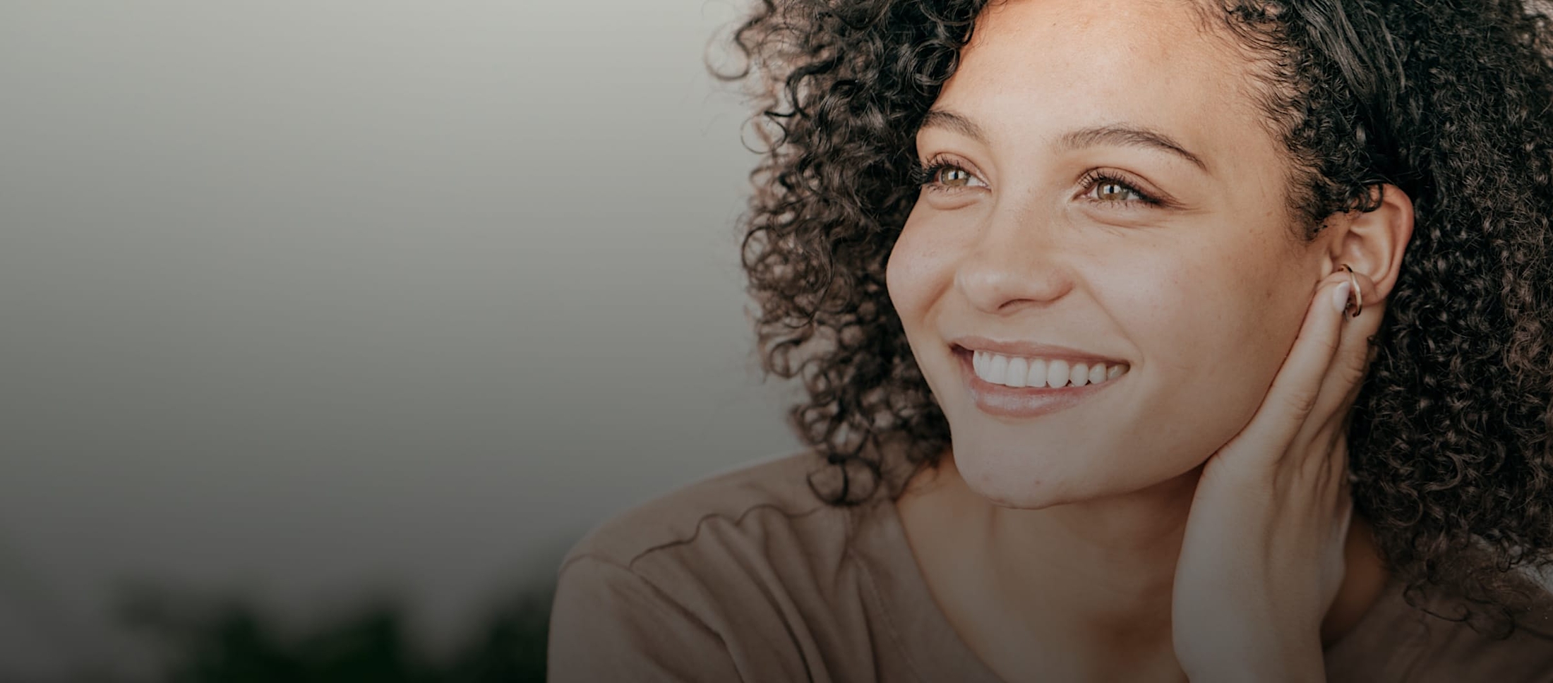 Woman with curly hair smiling, looking to the side