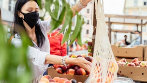 Woman in mask shopping for peaches at market