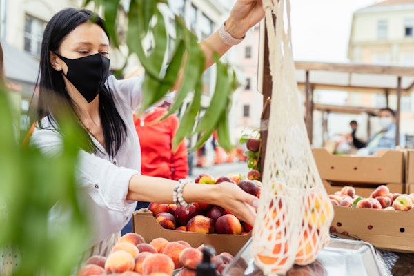 Woman in mask shopping for peaches at market