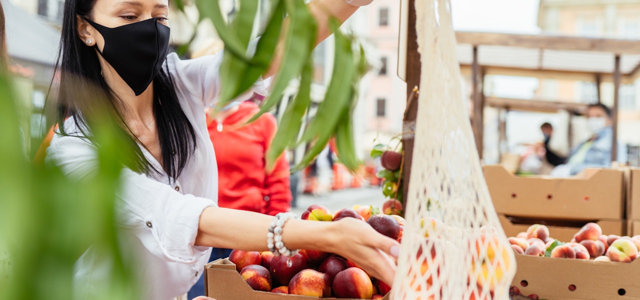 Woman in mask shopping for peaches at market