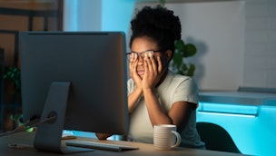 A-woman-sitting-at-a-computer-and-rubbing-her-eyes-at-night