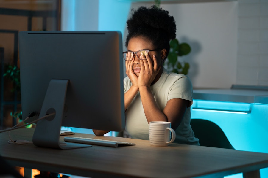 A-woman-sitting-at-a-computer-and-rubbing-her-eyes-at-night