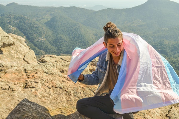 person-on-mountaintop-with-trans-flag