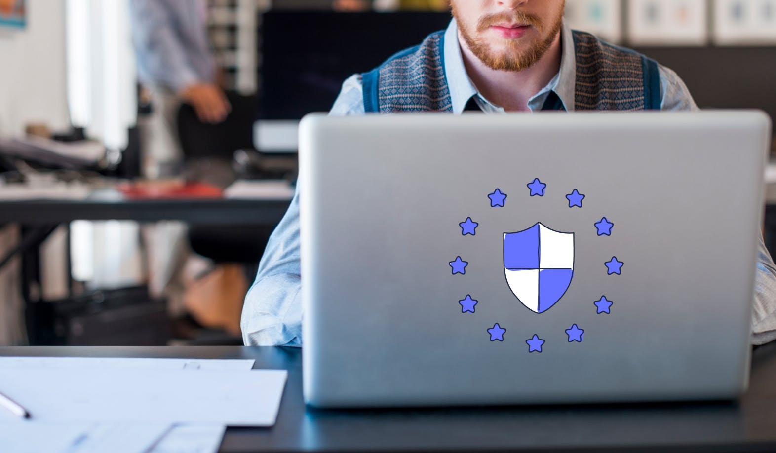 blogpost-image of a man behind his laptop and on his laptop is an illustration of a security shield surrounded by the GDPR stars