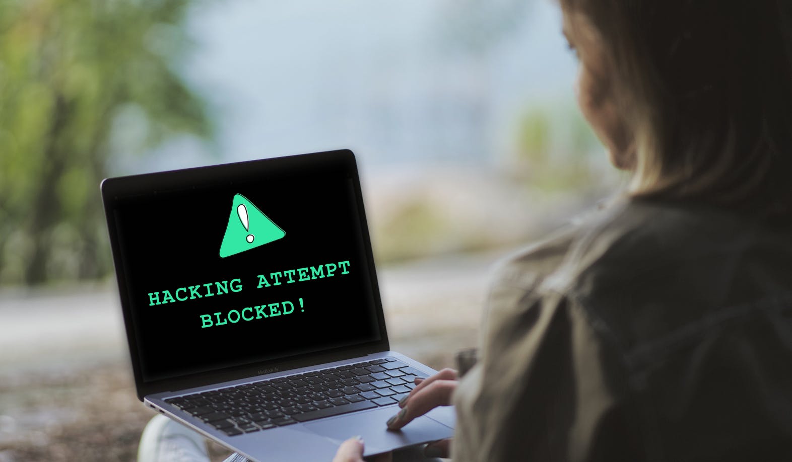 A computer screen with a StartMail brand style illustration of a warning sign with the text “hacking attempt blocked!”. 
