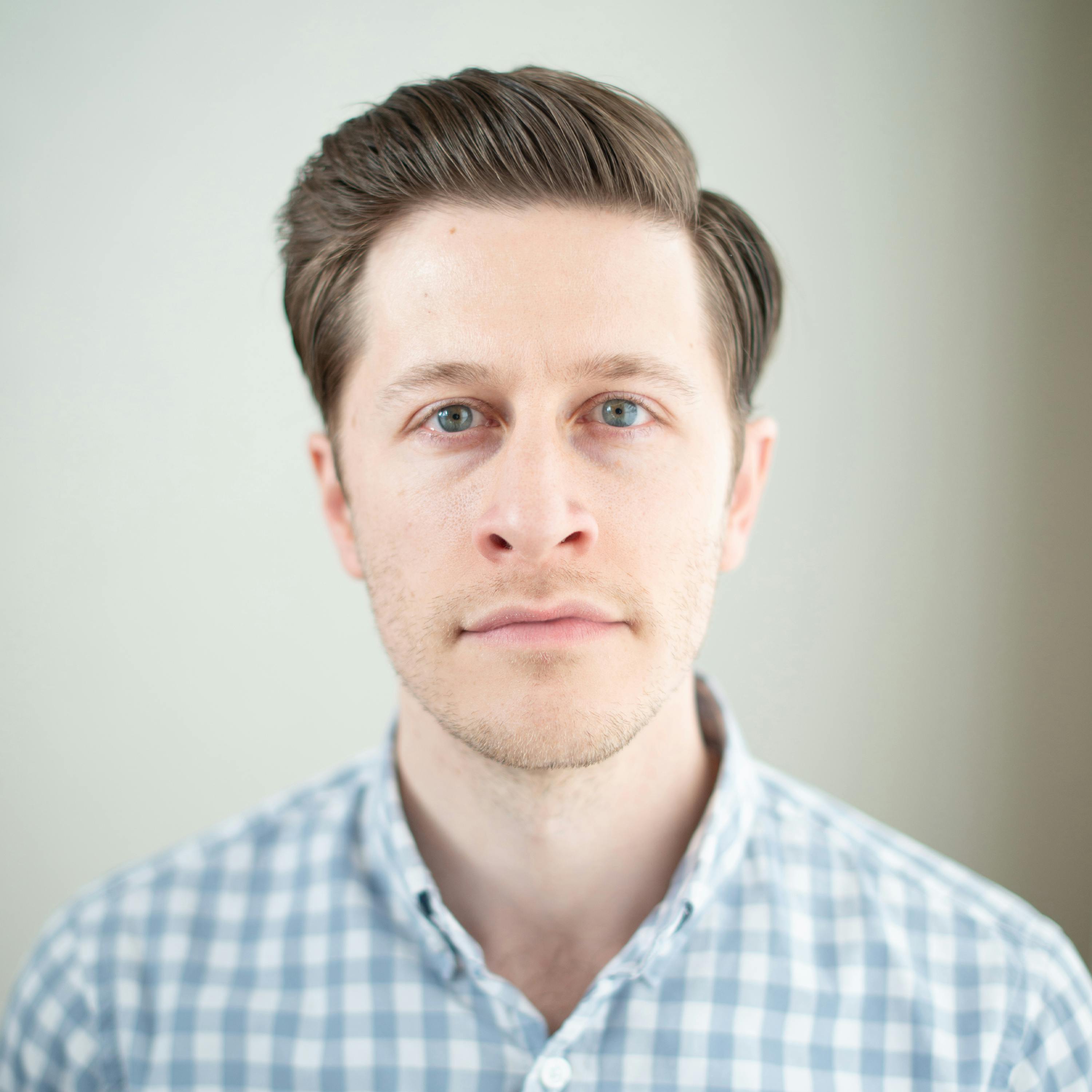 A headshot photograph of David Pakman, a progressive American talk show host and commentator. Pakman is shown facing the camera with a serious expression, wearing a dark suit and a light blue shirt. He has short brown hair and is seated against a light grey background.