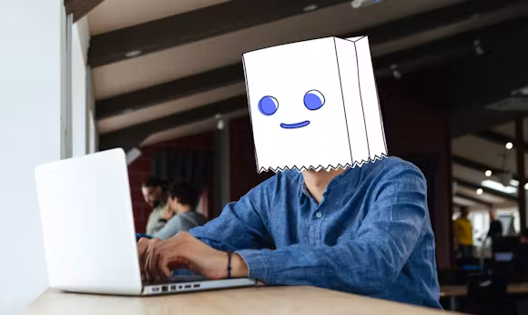 Photographic image of a man behind his laptop. In the StartMail illustration style a paper bag with an illustrated face representing Bagman, representing being anonymous.