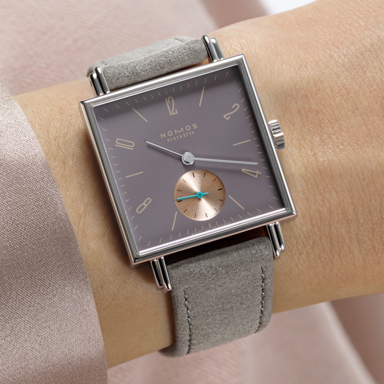 Nomos Tetra Die Fuchsteufelswilde - Uhr mit lilafarbenen Zifferblatt und grauen Lederband an einem Handgelenk