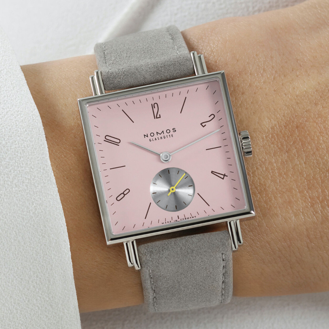 Nomos Tetra Die Wildentschlossene - Uhr mit rosafarbenen Zifferblatt und grauen Lederband an einem Handgelenk