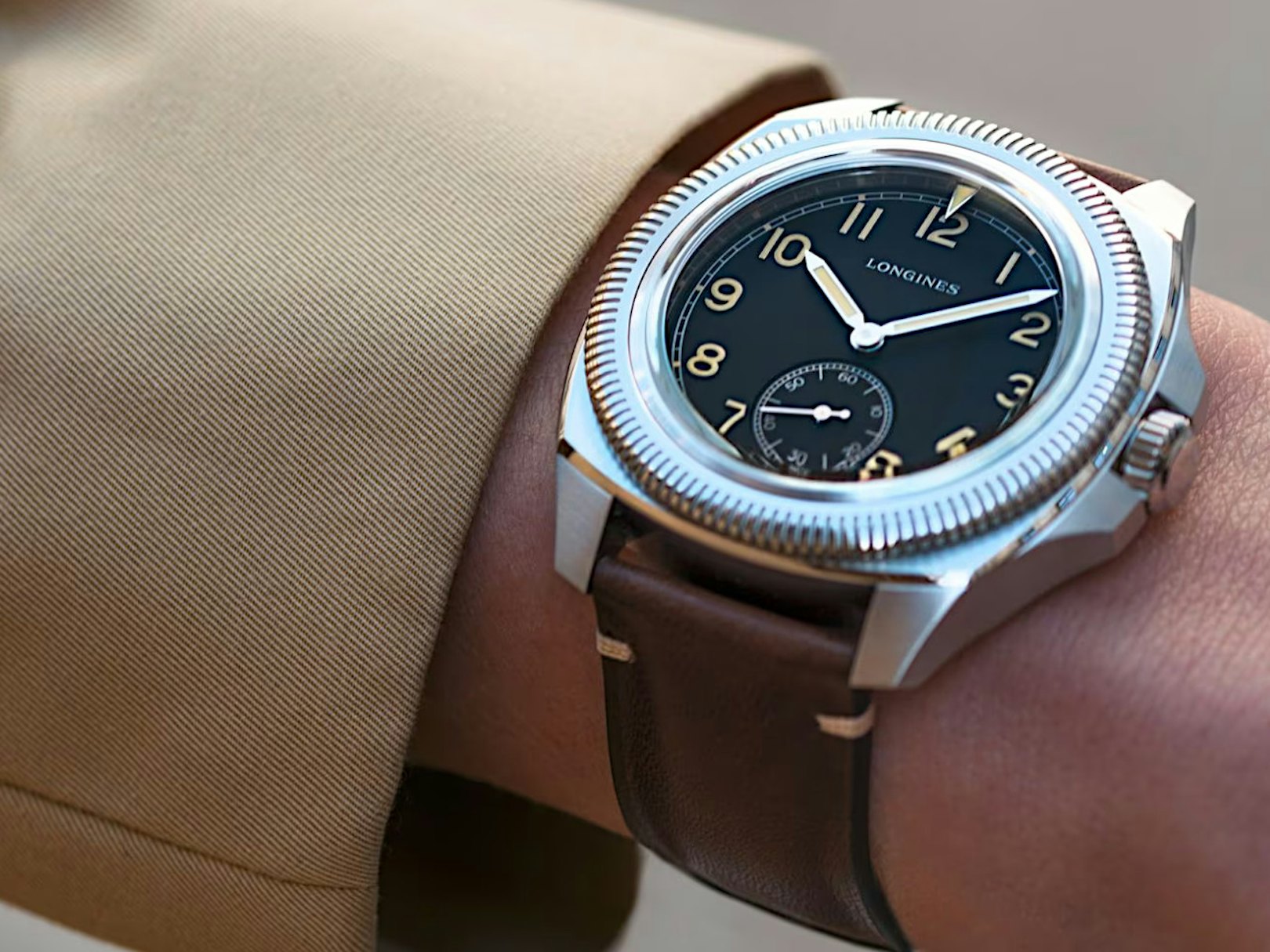 Longines Pilot Majetek - News Galerie - Uhr mit schwarzem Zifferblatt mit braunem Lederband an einem Handgelenk