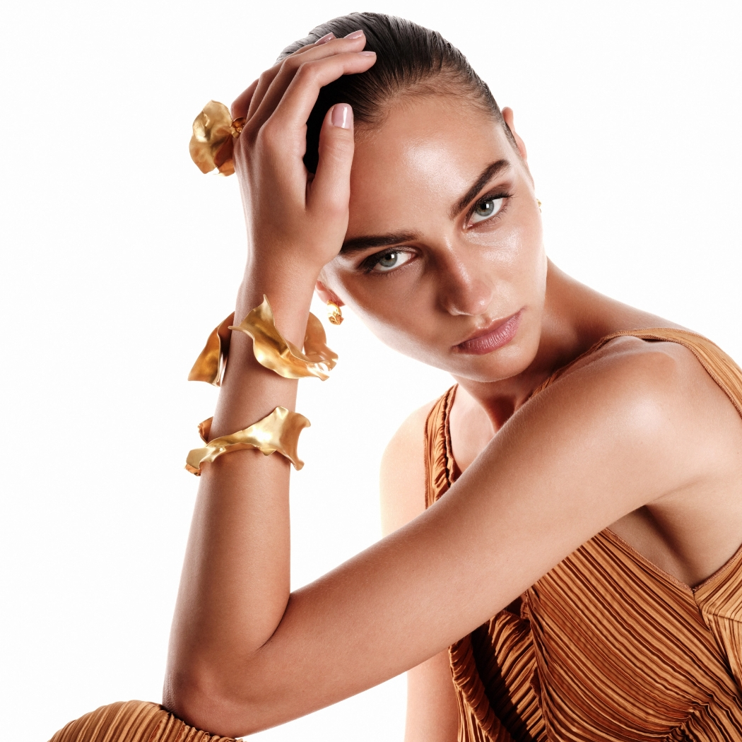 TheodoraD Markenbild - Goldschmuck am Hangelenk einer Frau mit orangener Kleidung