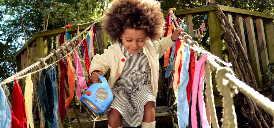 Girl playing on treehouse holding the Yoto Player