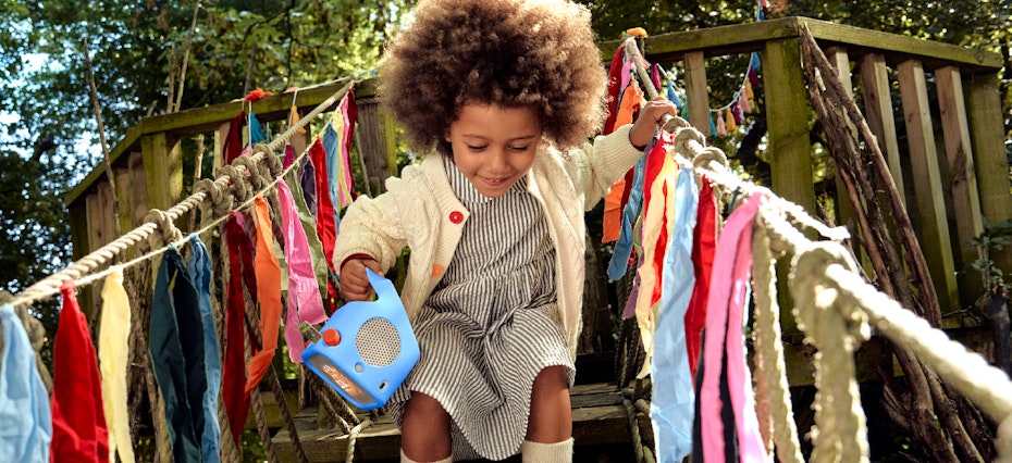 Girl playing on treehouse holding the Yoto Player