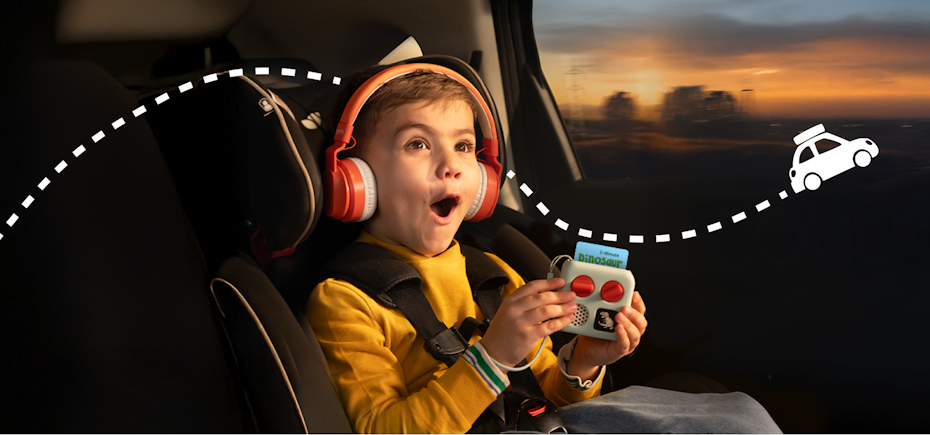 Child in car holding the Yoto Mini, Wearing the Yoto Wireless Headphones