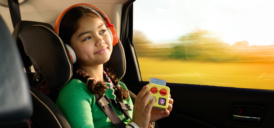 Child in a car seat using a yoto mini with headphones