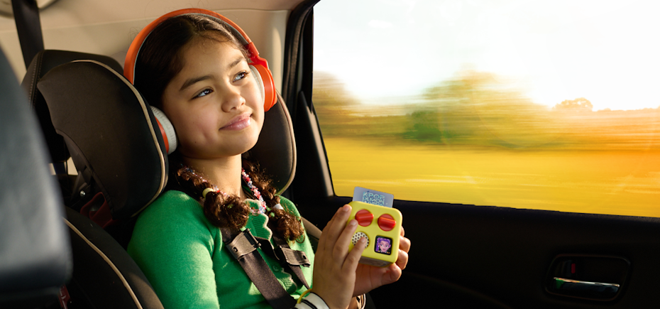 Child in a car seat using a yoto mini with headphones