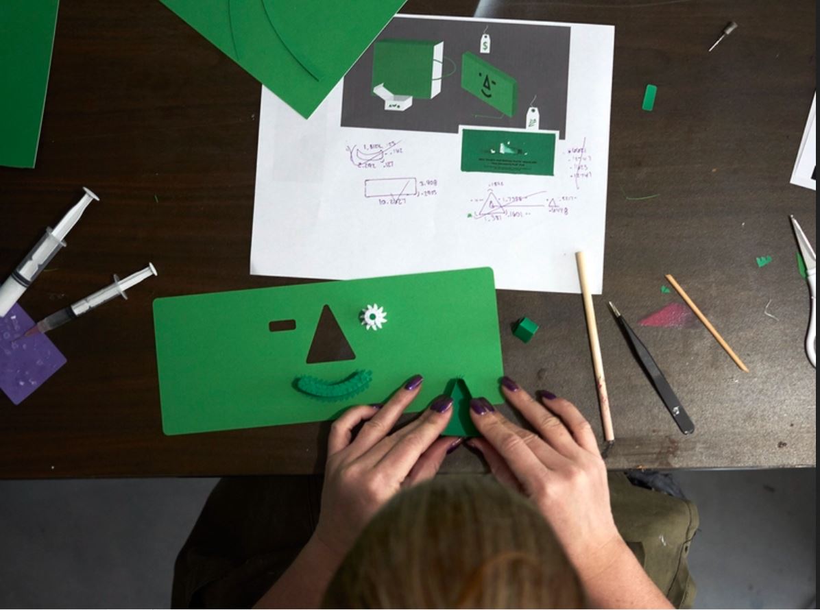 A woman creates a mock of her final project with a green cardboard paper