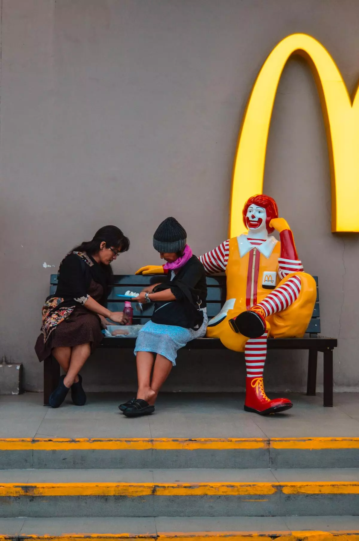 Two women are dining on the bench with McDonald’s mascot