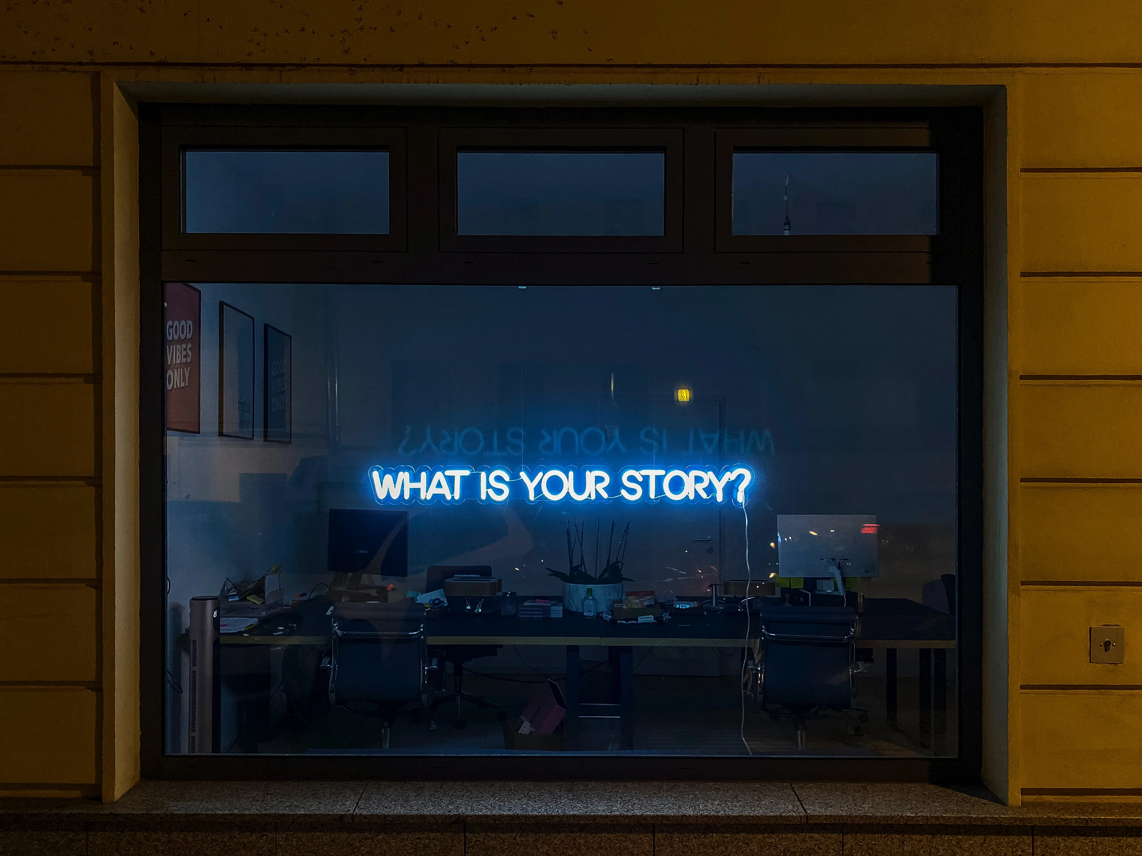 A neon sign that says “What is your story?” can be seen on a glass window.
