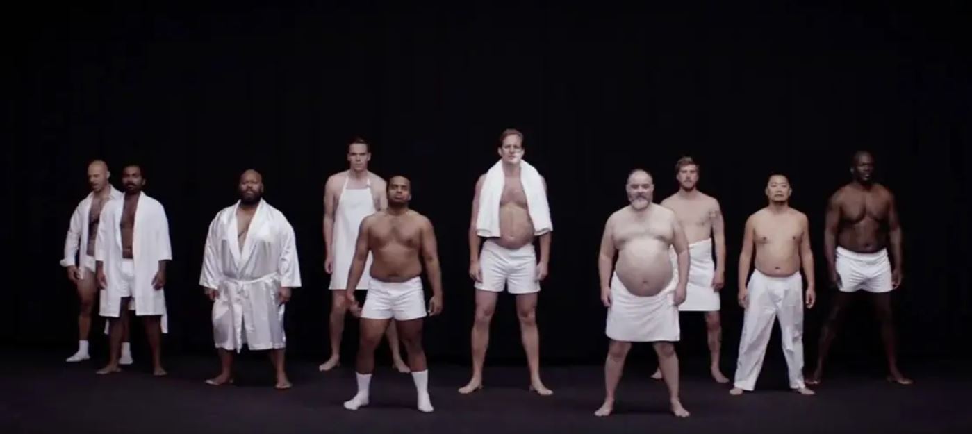 A group of men in towels and robes stands in a dark room