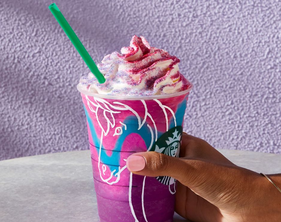 A woman holds a cup of colorful frappuccino in pink, blue, and purple