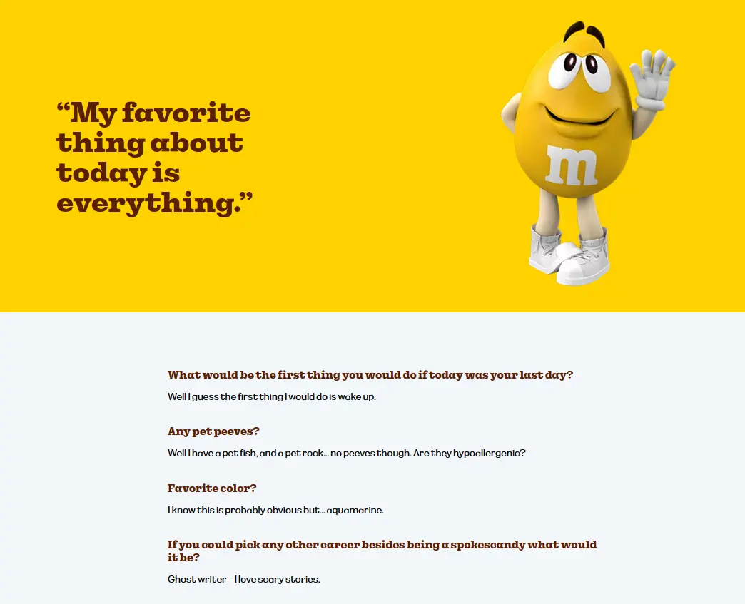A yellow M&M’s mascot shyly waves hello