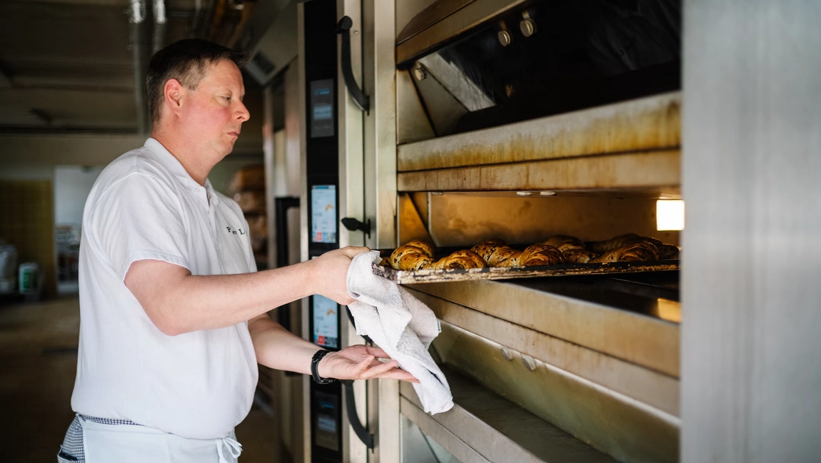 A baker brings out a tray of bread fresh from the oven