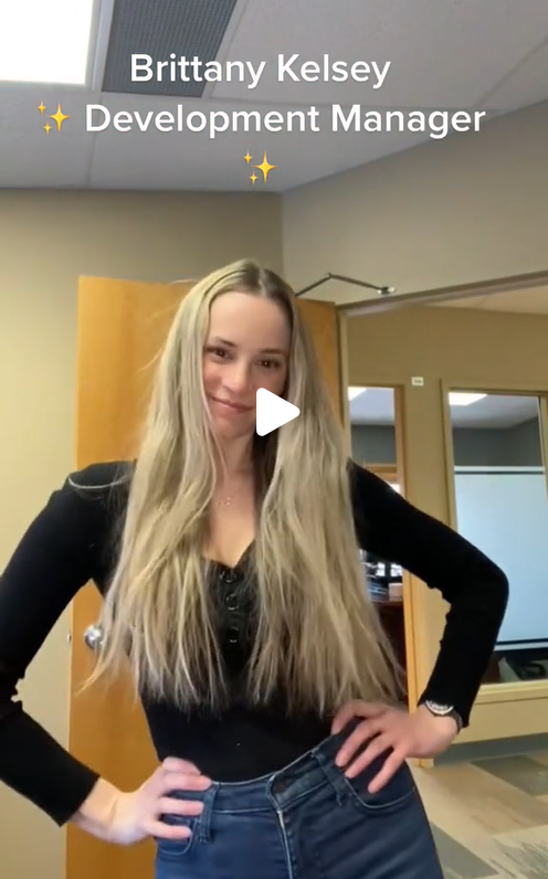 A woman in a black top and jeans stands with her hands akimbo