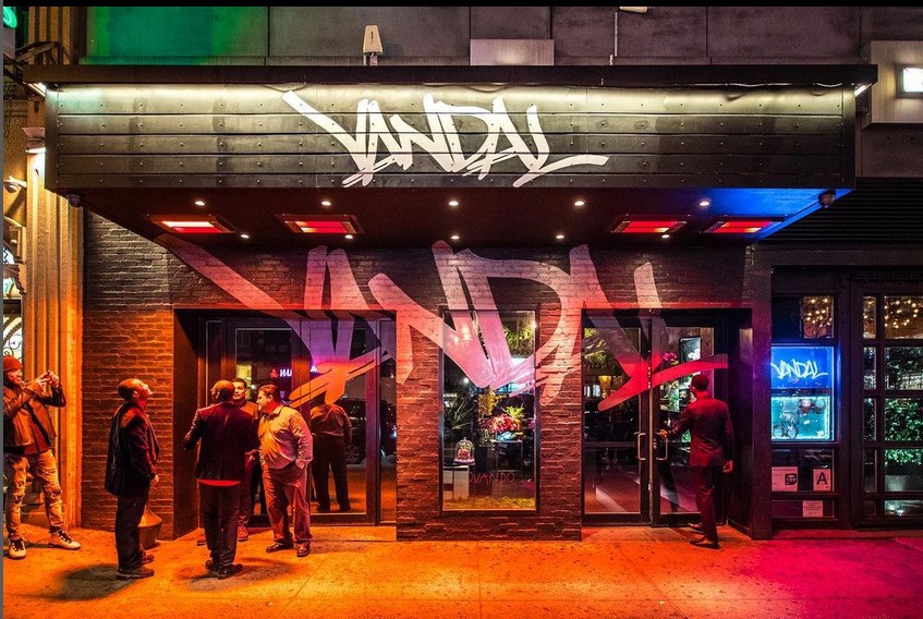 A group of men standing in front of a restaurant with graffiti on the wall