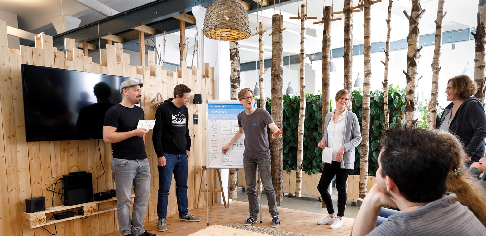 Personen aus dem brainbits-Team stehen im Open Space am Whiteboard und tragen etwas vor.