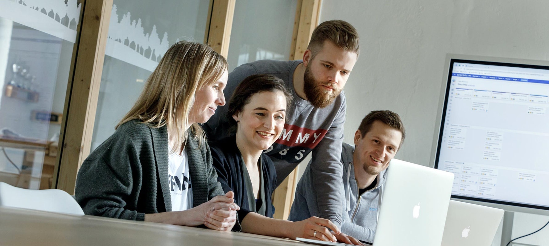 Vier Mitarbeitende von brainbits sitzen im Konferenzraum und schauen gemeinsam und lächelnd auf den Bildschirm eines Laptops.