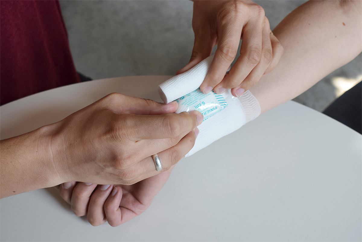 Zwei Hände wickeln einem Arm einen Verband um.