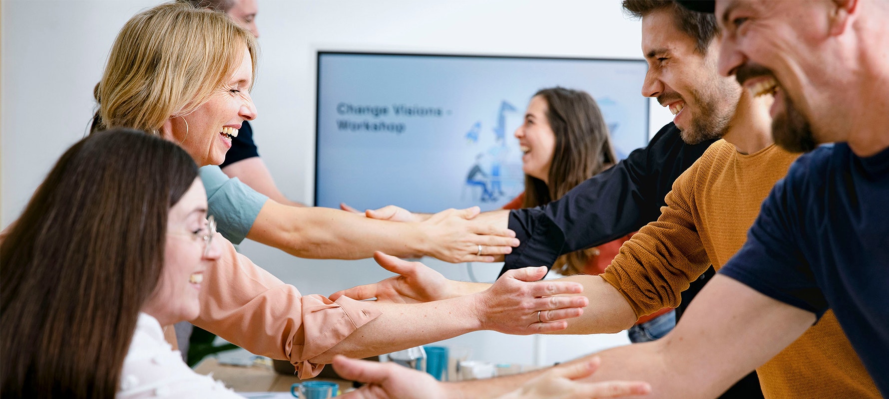 Je drei Personen stehen sich lachend im Konferenzraum gegenüber und klatschen einander ab.