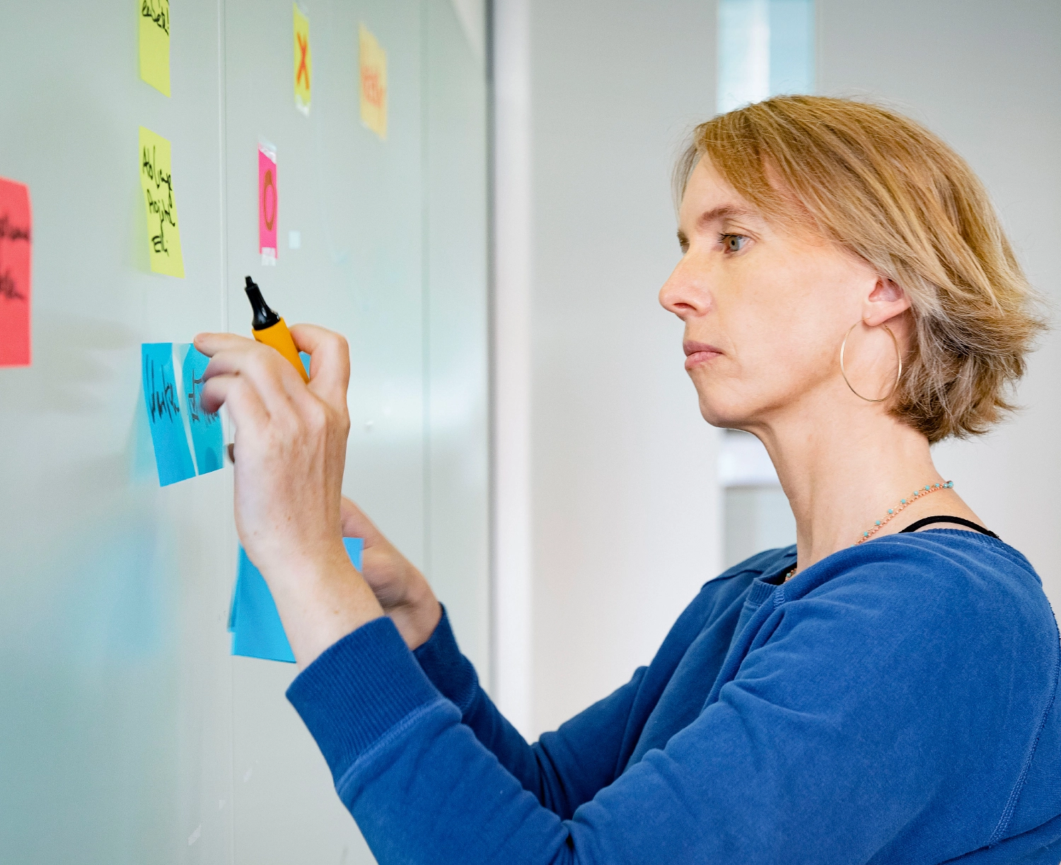 Scrum Masterin Bettina Kuchenbuch beschriftet Post-its an einer Glaswand.