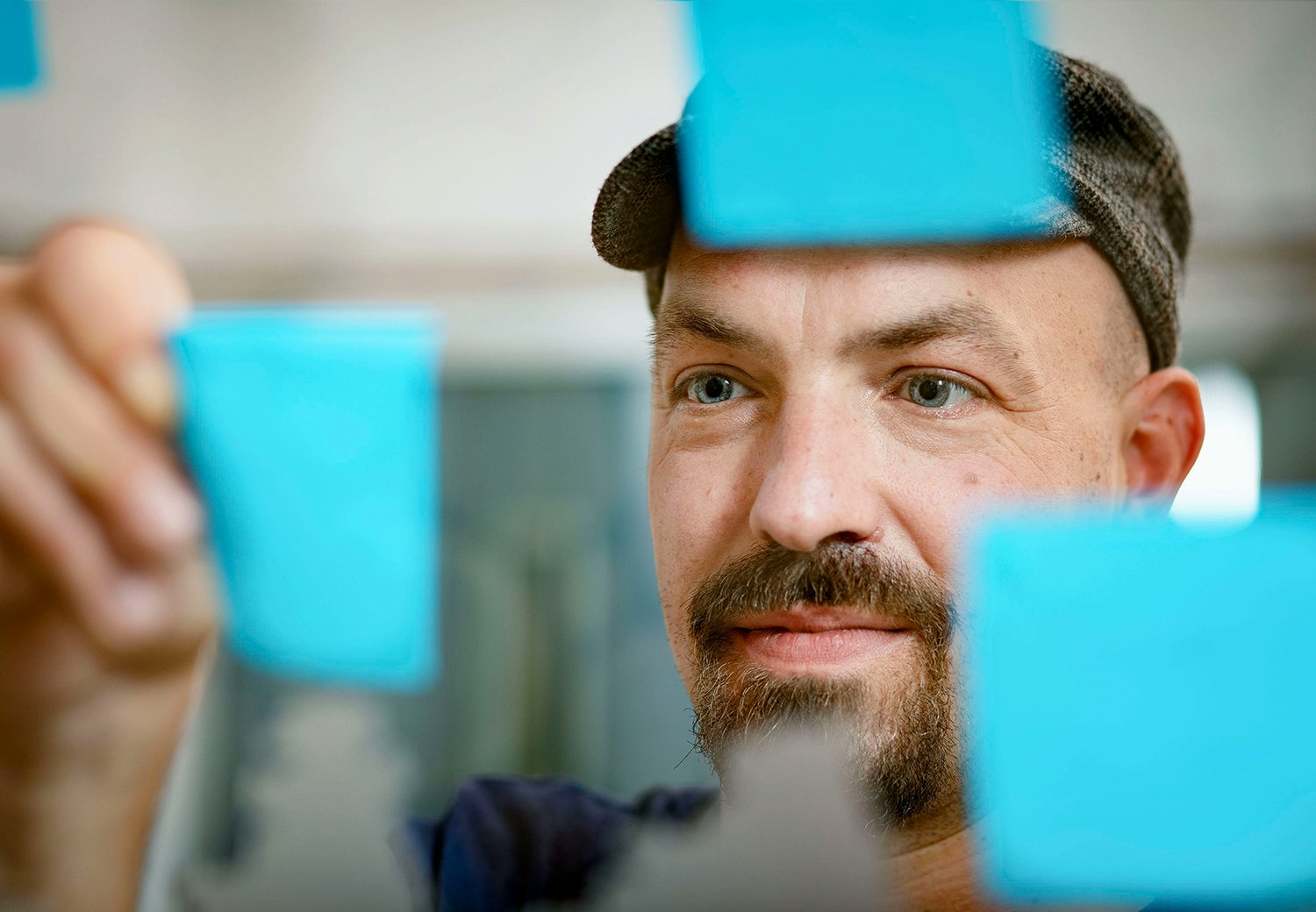 Agile Coach Marian Bosse von vorn, wie er blaue Post-Its an einer Glasscheibe befestigt.