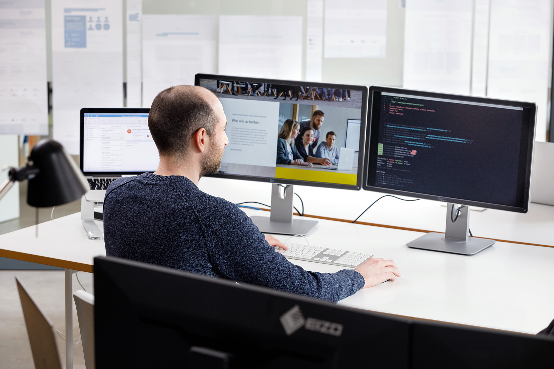 Foto: Softwareentwickler sitzt vor zwei Bildschirmen an einem Schreibtisch.