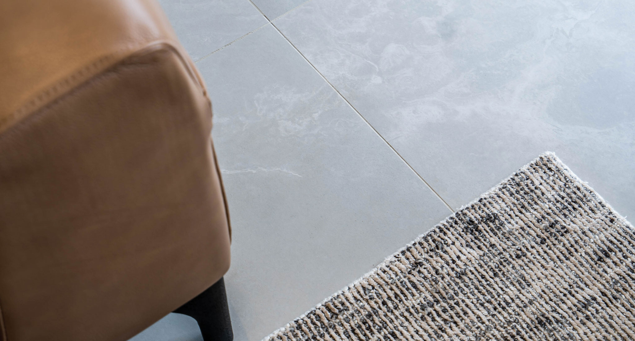 Close up image of iridescent Stardust Moon tiles which mimic the look and movement of marble. On the bottom right, a glimpse of a textured rug can be seen and on the left the edge of a leather ottoman. 