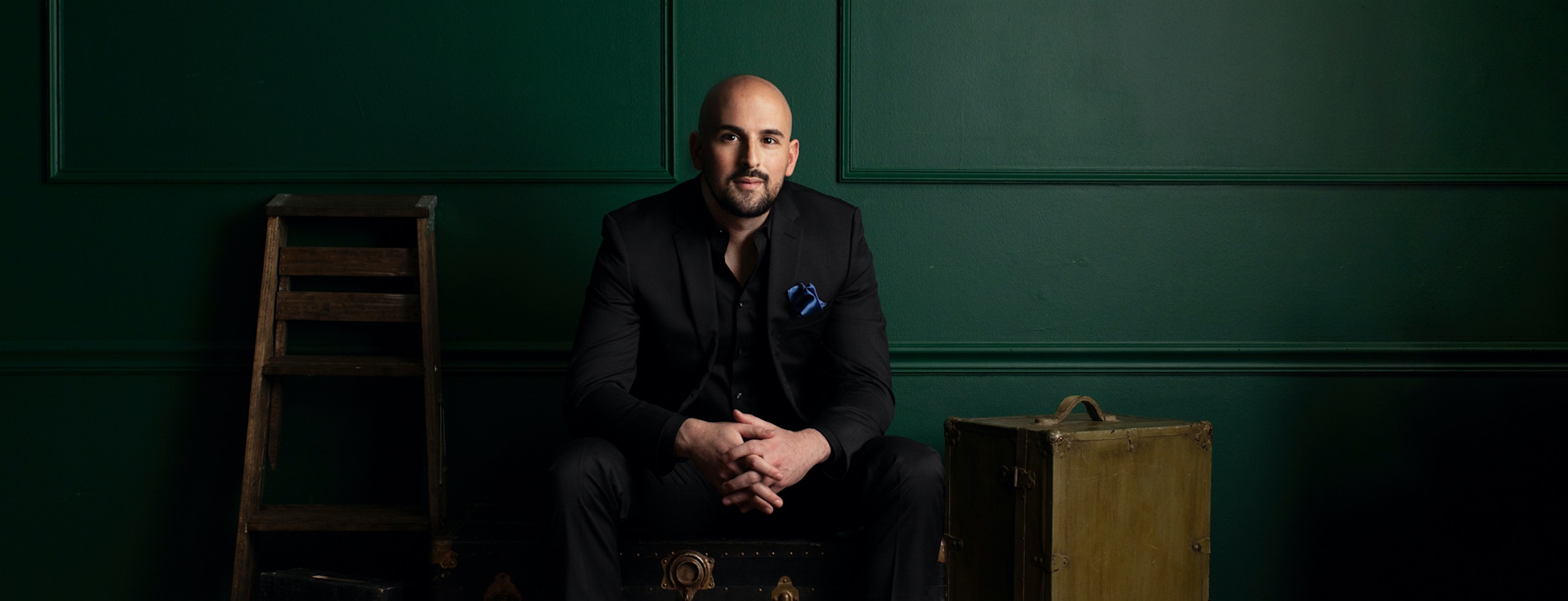 Dr. Edward Chamata in black suit posing for photo in front of green wall