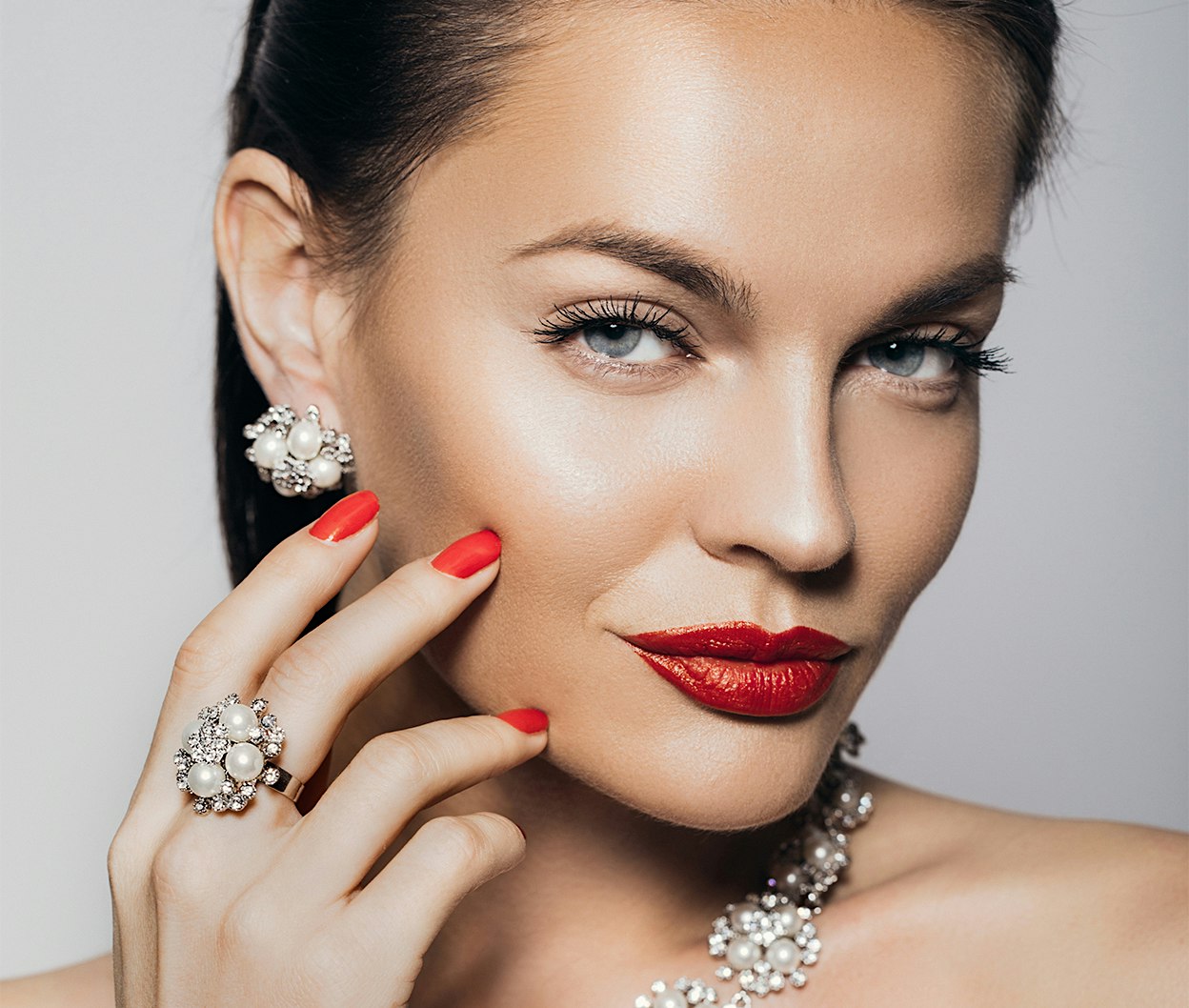close up of a woman with red nails, necklace, and earrings