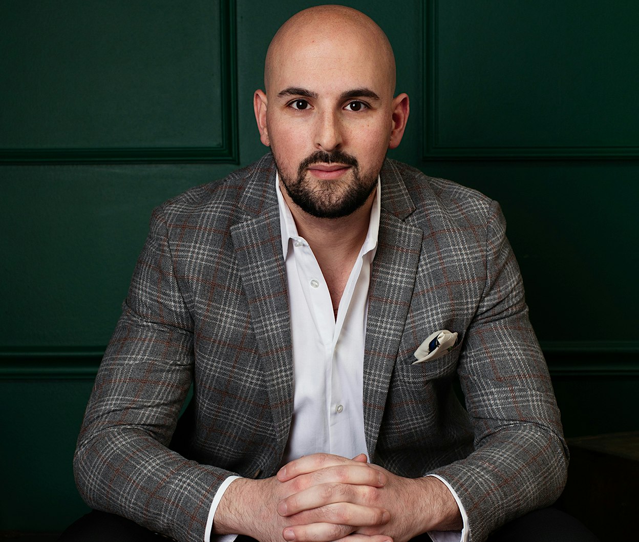 Dr. Edward Chamata in checkered blazer and white button up shirt sitting and leaning forward for photo