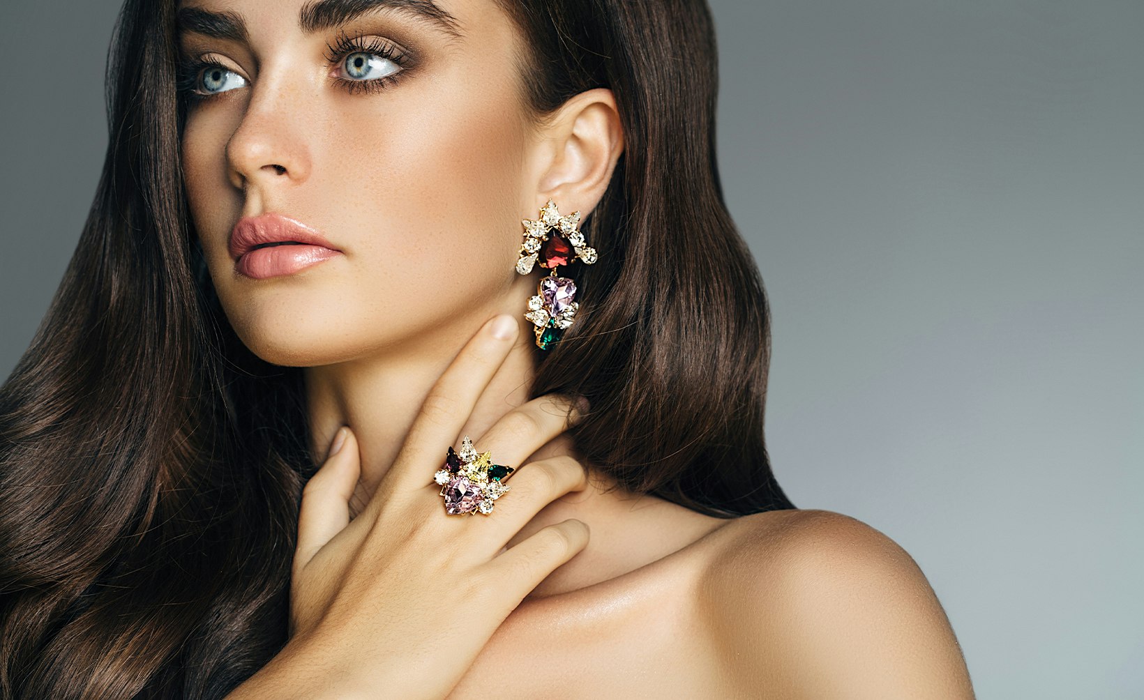 woman with long brown hair posing for picture with wearing a pair of earrings with her hand on her neck