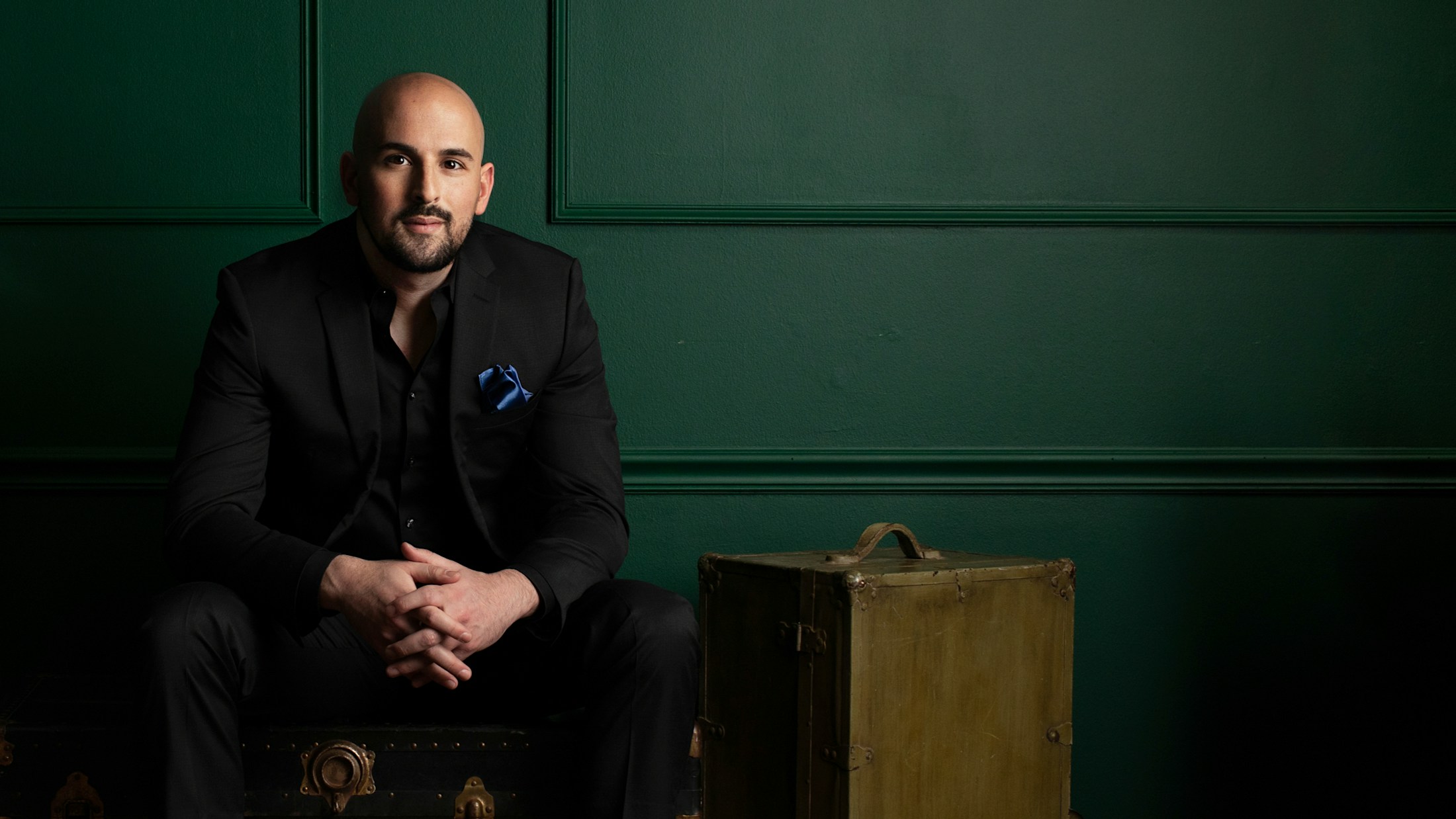 Dr. Edward Chamata in a black suit sitting in front of a green wall