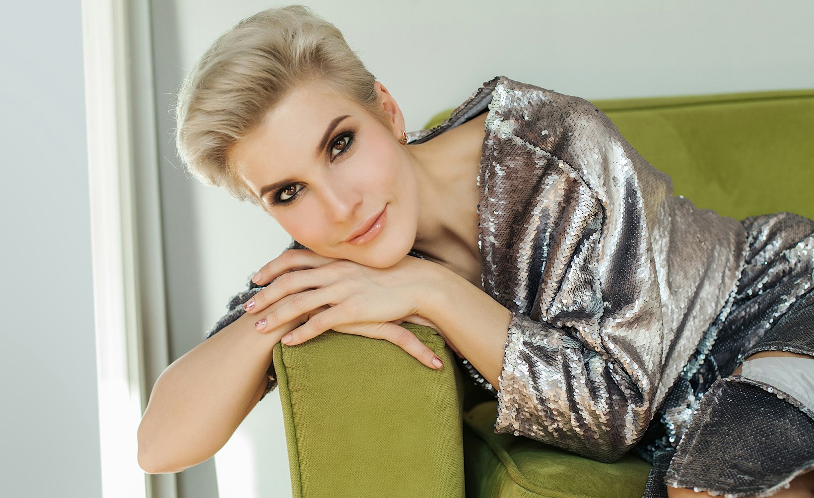 blond woman in silver dress sitting on green chair with hand on arm