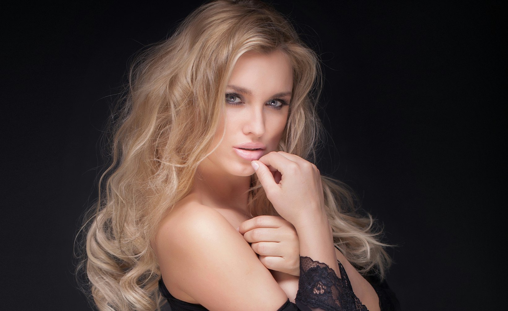 blond woman with long hair posing in black dress with finger on lips