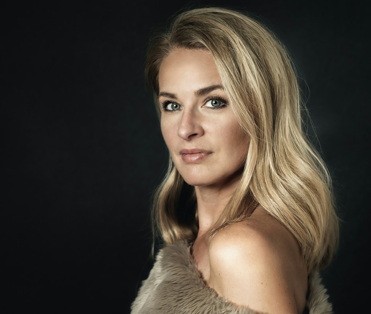 blond woman with blue eyes and a fur coat posing for a picture