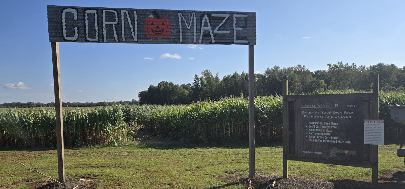 entrance to a corn maze sign in front of a corn field