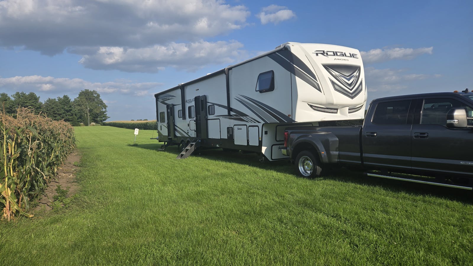 truck and fifth wheel camper parked in grass beside a corn field
